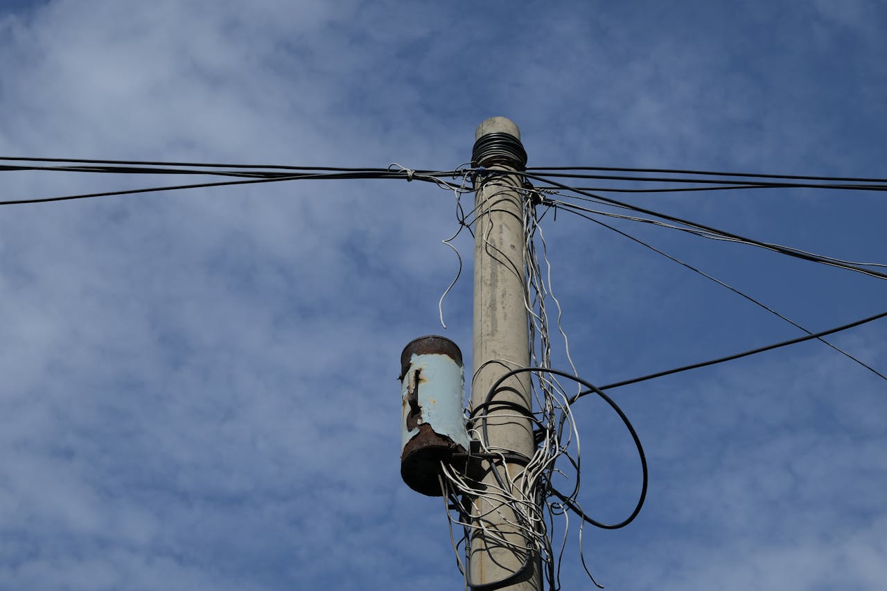 About Photograph of a utility pole and power lines under a bright blue sky with scattered clouds.